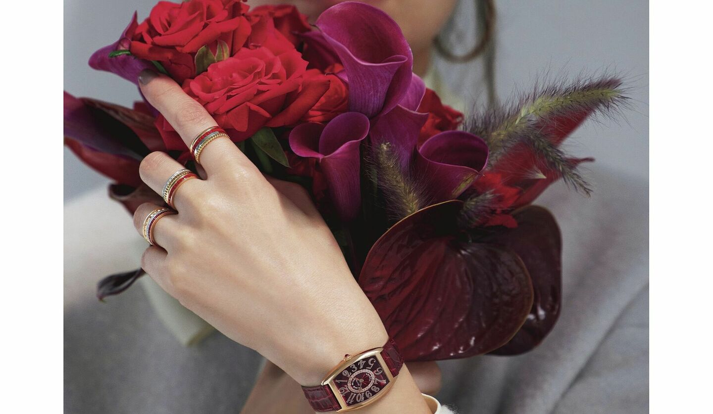 赤い花束に「ブシュロン」の時計や指輪を付けた手の写真