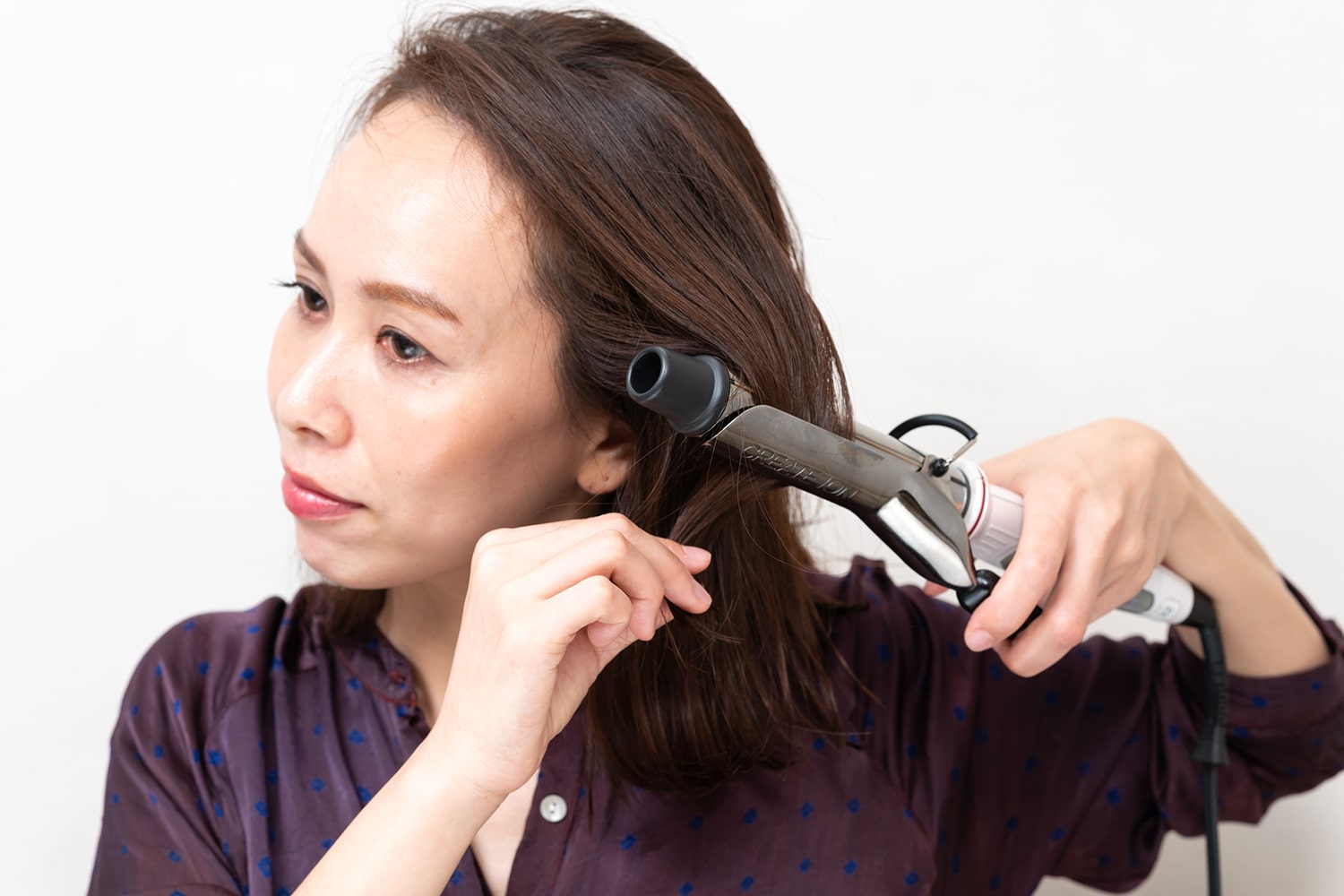 コテは32mmを使用。毛束を挟んで毛先を持ち、コテを外側に押し出すように熱を当てる。