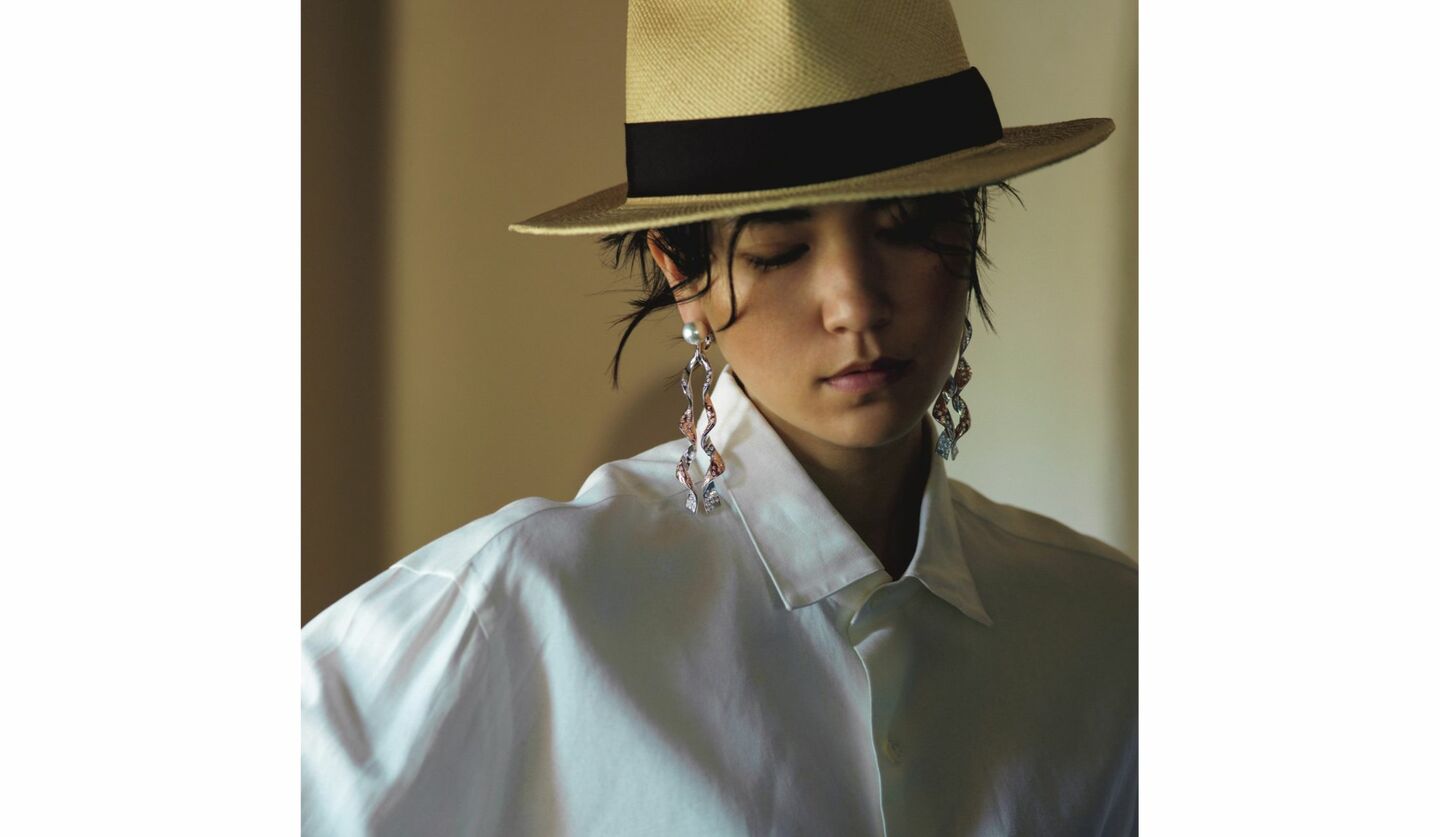 麦わら帽子に白シャツと「TASAKI」真珠ピアスをした女性の写真