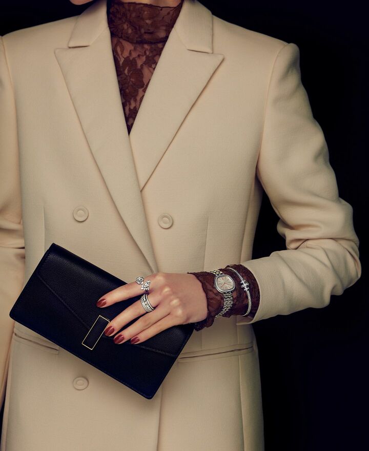 「ヴァレクストラ」のクラッチバッグと「ピアジェ」のジュエリーを纏った女性の手元