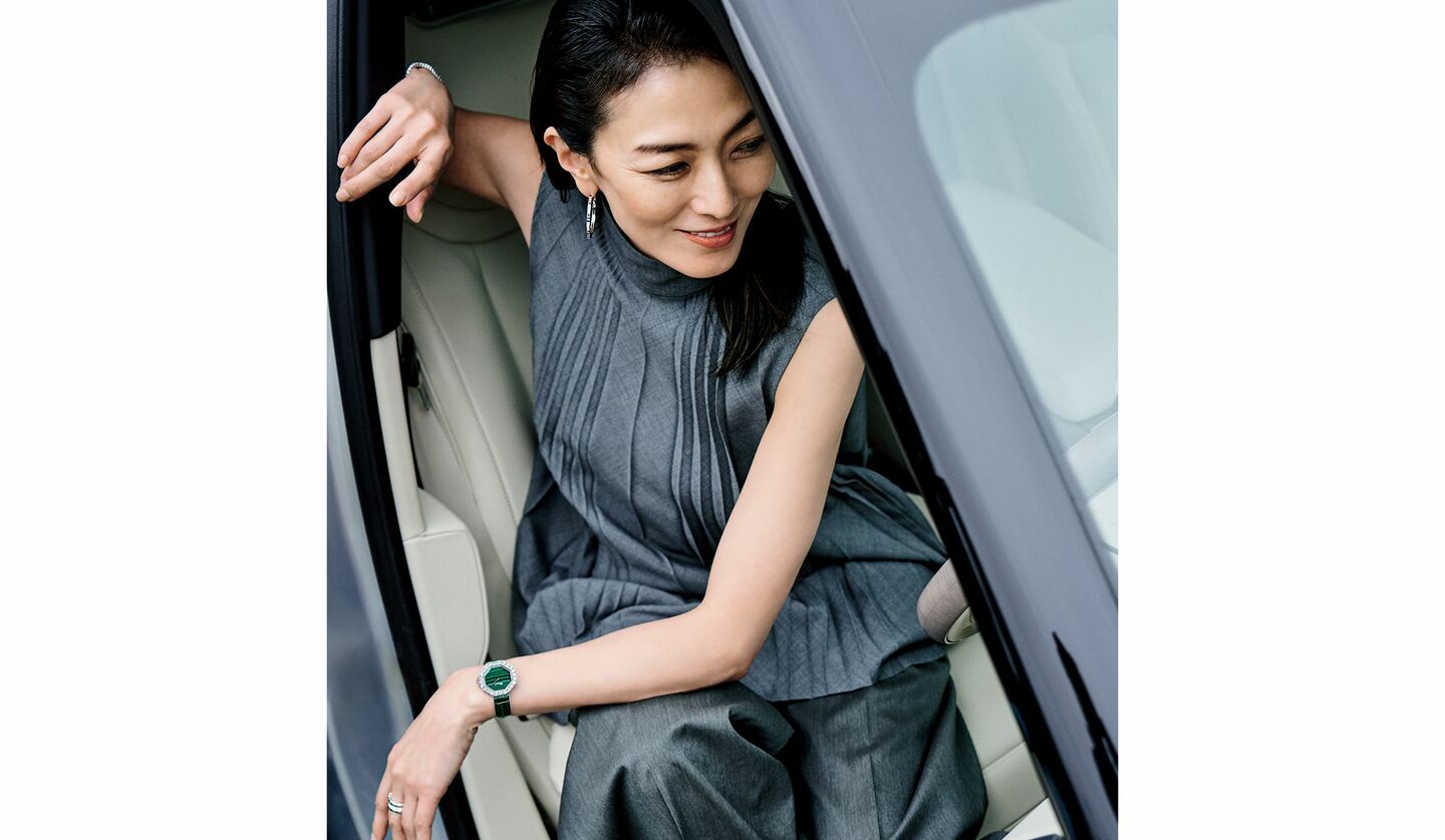 グレーのパンツスタイルと「ショパール」の時計を着用して、自動車の運転席に座る板谷由夏さん