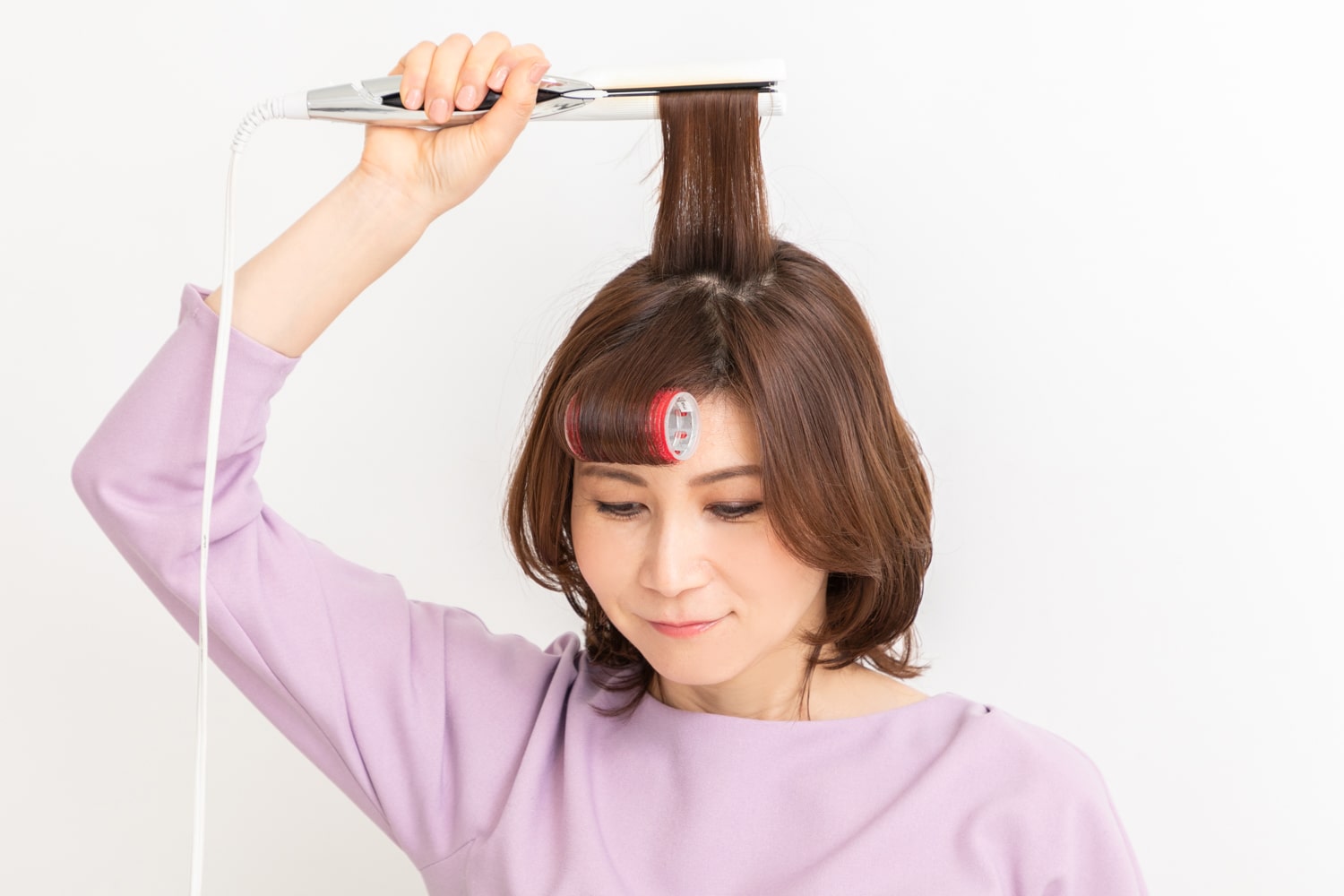 頭頂部の髪を取り、ストレートアイロンを根元~毛先まですべらせて丸みをつける。カーラーを外し、毛先のみオイルをつけて束感を出したら完成。