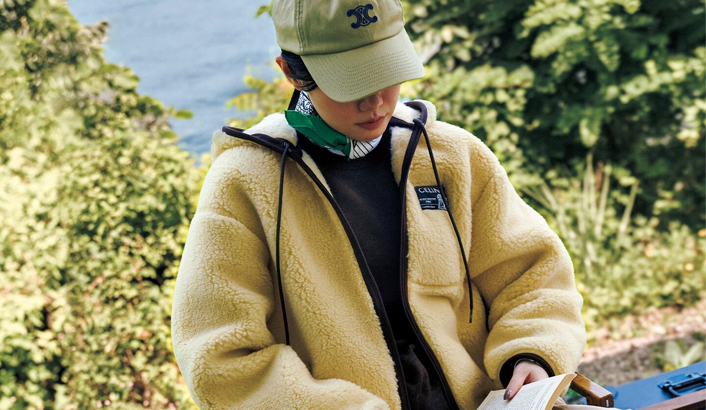 セリーヌのボアジャケットを着用して水辺で本を読むモデル