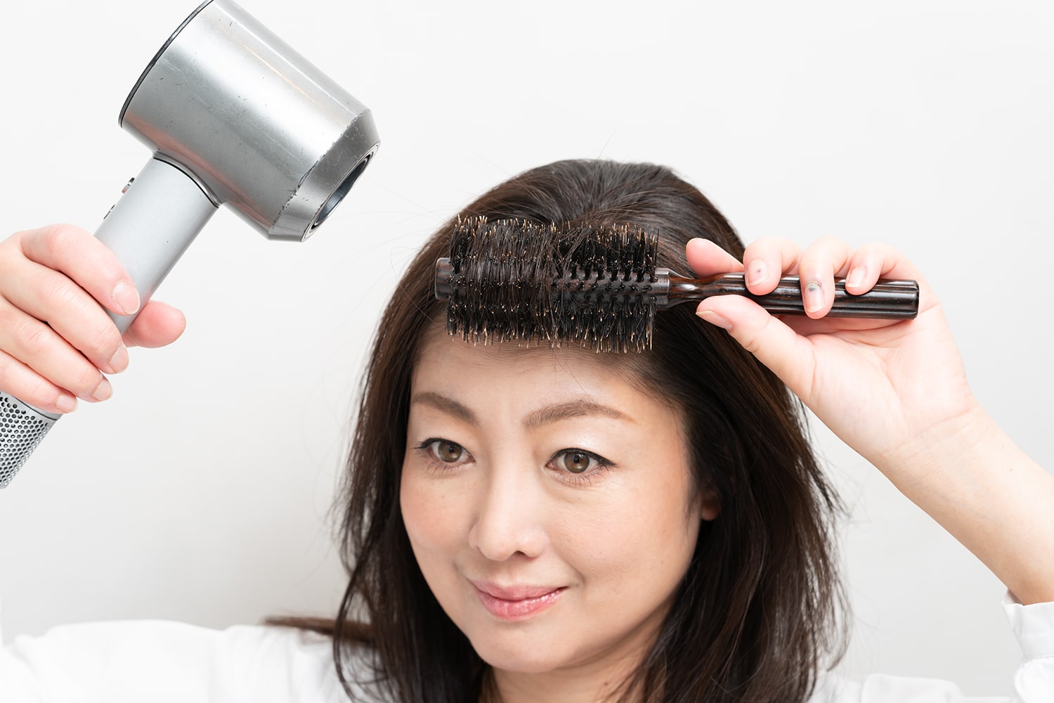 ブラシに前髪を巻きつけてドライヤーの熱を当てる。根元までしっかりと巻きつけて。