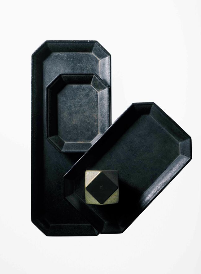 ●『真鍮の文具トレイ』（黒ムラ）左：大［縦21×横8.7㎝］￥5,500・上に重ねたトレイ：小［縦8.7×横７㎝］￥3,500・右：中［縦14×横8.7㎝］￥4,250・右のトレイの上：『ペーパーウェイト』（鋳肌）四角［縦横3.5×高さ3.5㎝］￥3,000 黒ムラ、鋳肌とも、使い込むことで深まる味わいを楽しみたい。〝フタガミ〟は明治30年創業の富山県高岡市の真鍮鋳物メーカー「二上」が立ち上げたブランド。（二上）