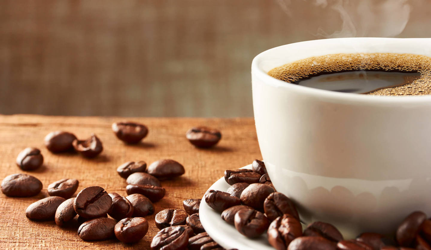 白いソーサー付のマグカップに湯気がたつコーヒーが入れられ、その周りにコーヒー豆が散らばっている