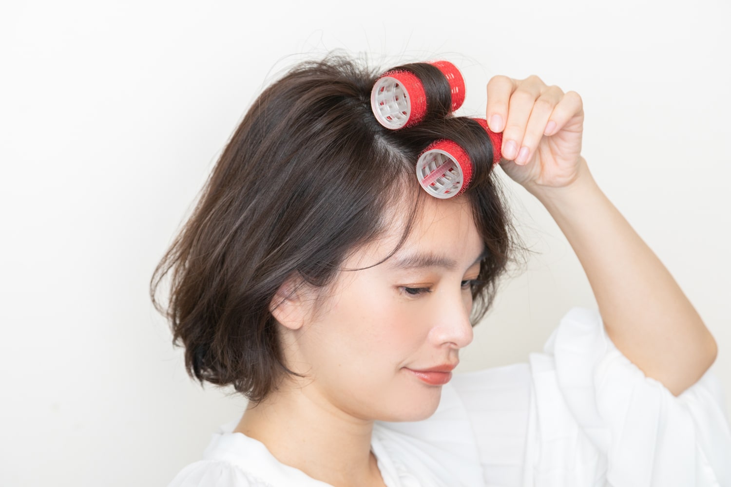 分け目をまたぐように、カーラーでトップと前髪を、前に向かって巻き込む。前髪の根元は、流すのと逆を向くように。