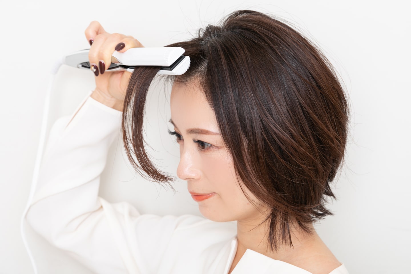前髪にストレートアイロンを当てる。少し根元を浮かせながら、根元から毛先に向かってすべらせる。