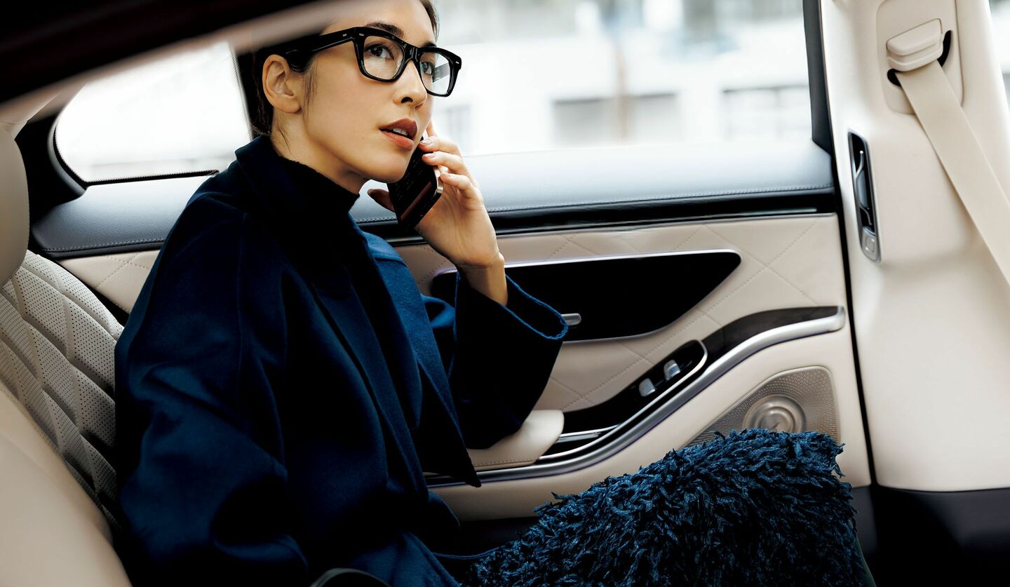 「アクリス」のフリンジスカートとコートを着用して、自動車内に座るモデル