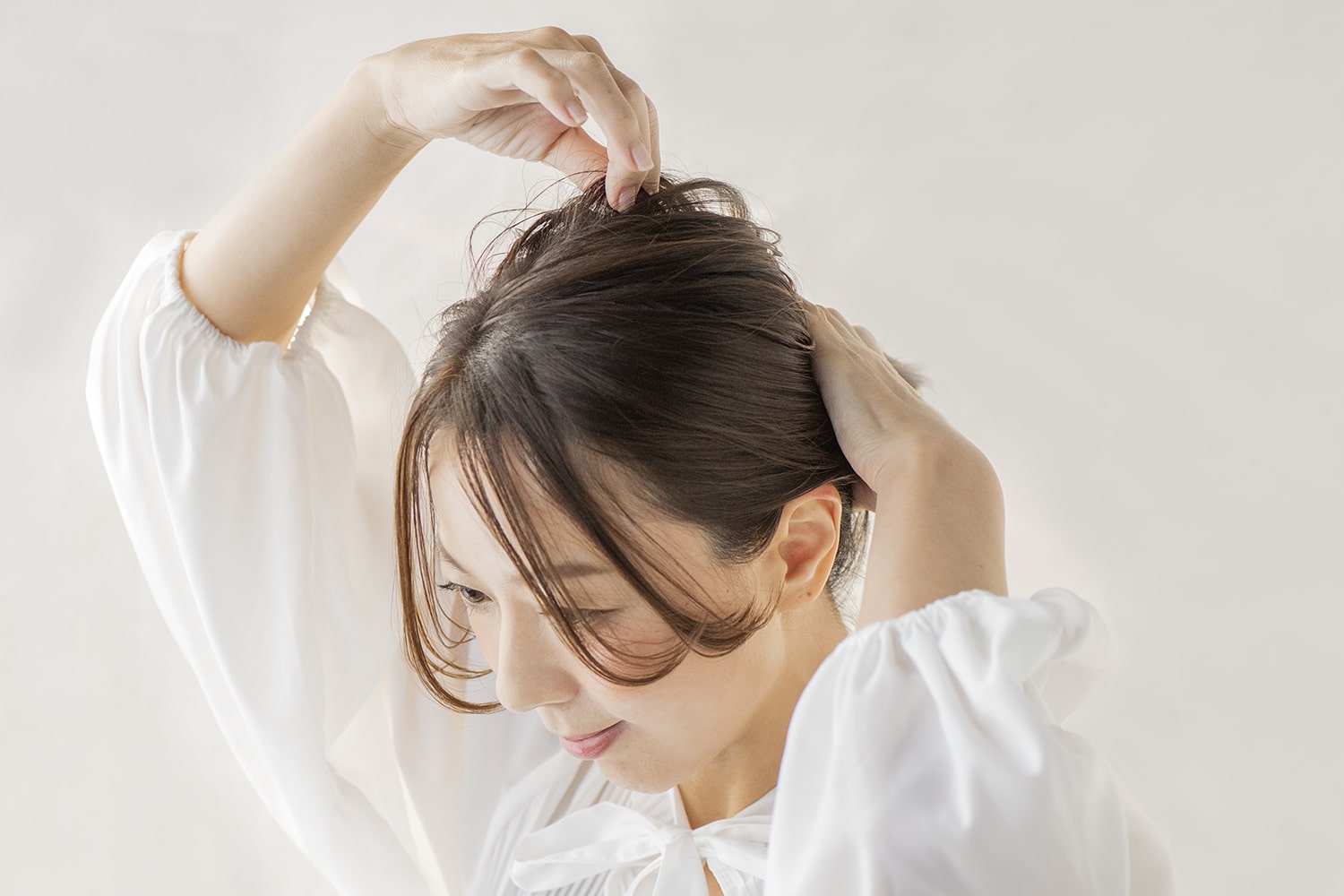 シニヨンの根元を押さえながら、後頭部に高さが出るように毛束を引き出す。