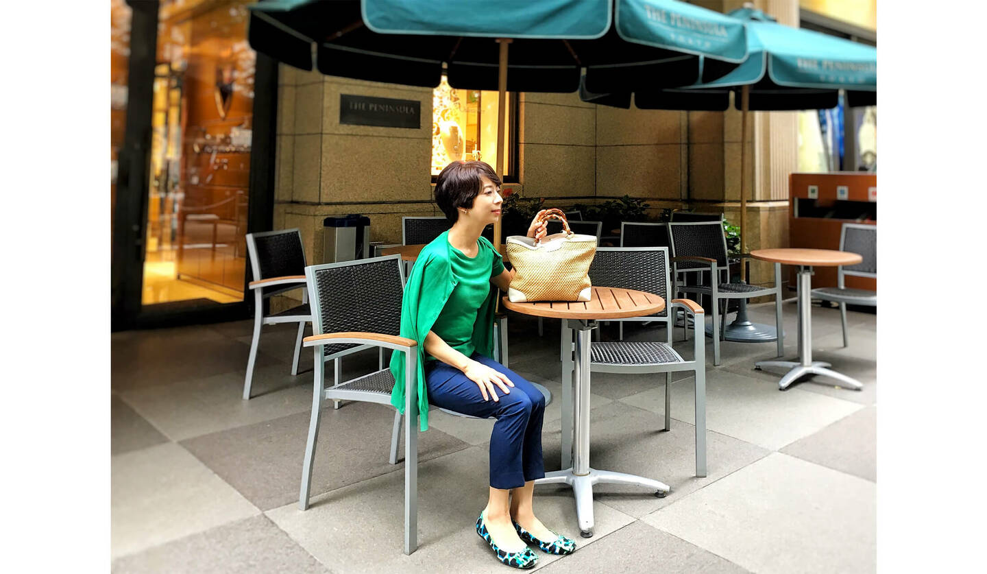 グリーンのツインニットとくるぶし丈のパンツを履いた女性がカフェに座っている図