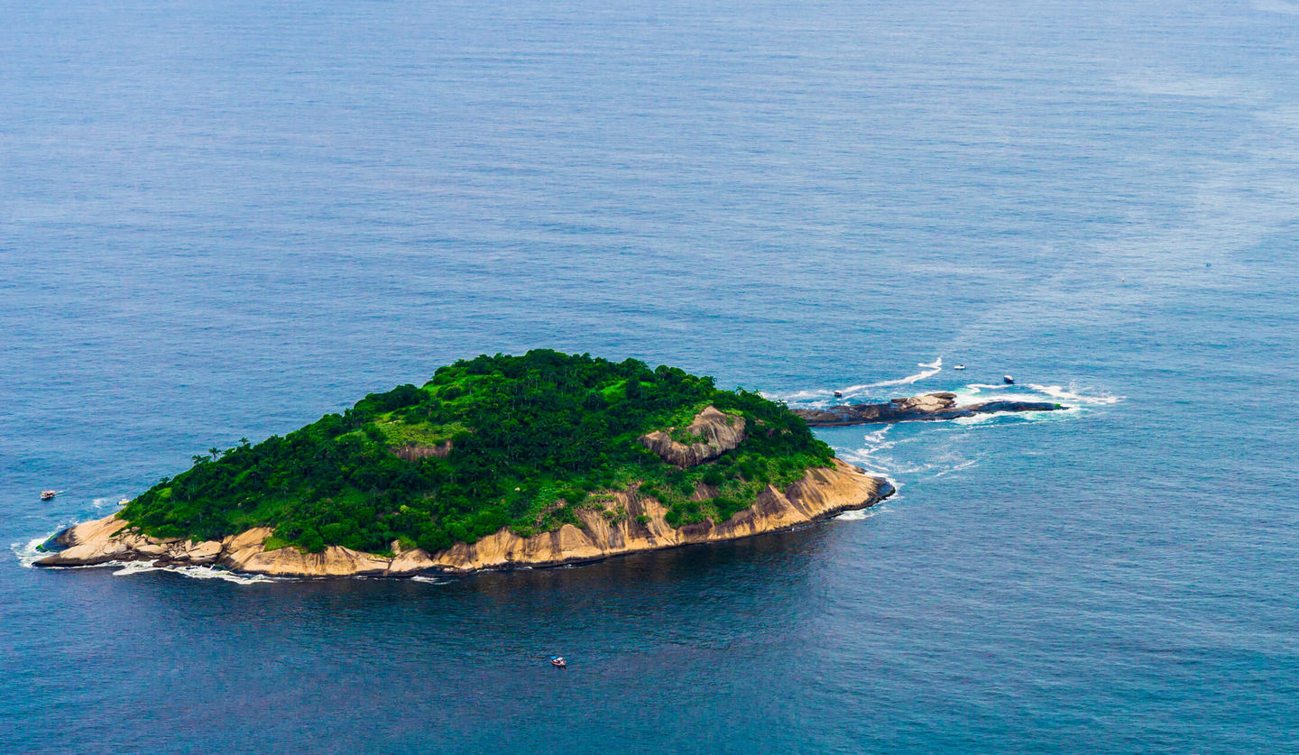 透明感のある青い海に浮かぶ緑が生い茂った無人島全体が上空から写されている