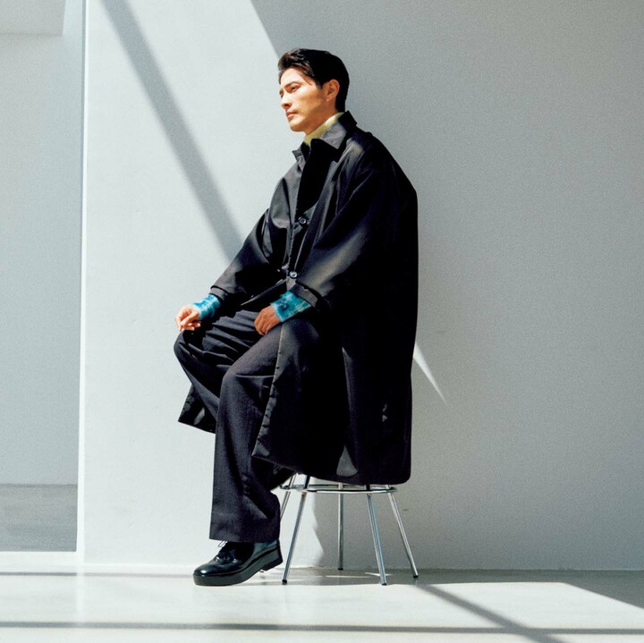 装いの主役は「プラダ リナイロン」のハリやコシを生かし、たっぷり感が際立つようなビッグシルエットのステンカラーコート。ランウェイではトップボタンまで留めて袖を肘より上まで捲り上げていたのが印象的だったが、やや短めの袖丈なのでそのまま羽織っても、インナーのモヘアのタートルネックニットがさりげなく覗いてアクセントになる。ゆったりしたワイドパンツも柔かなフランネル製ゆえ、全体のエアリーなシルエットが、より一体感を増し強調されるのだ。コート￥442,200［予価］・ニット・中に着たイエローのニット・パンツ／参考商品・靴￥149,600［予価］（プラダ クライアントサービス）