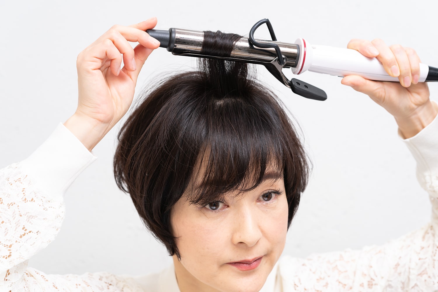 毛束を真っ直ぐ上に持ち上げながら、顔側の毛束は毛先から内巻きに、後頭部側の毛束は外巻きにする。