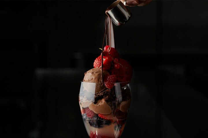 銀色のミルクピッチャーに入ったホットチョコレートをパルフェの上からかけている