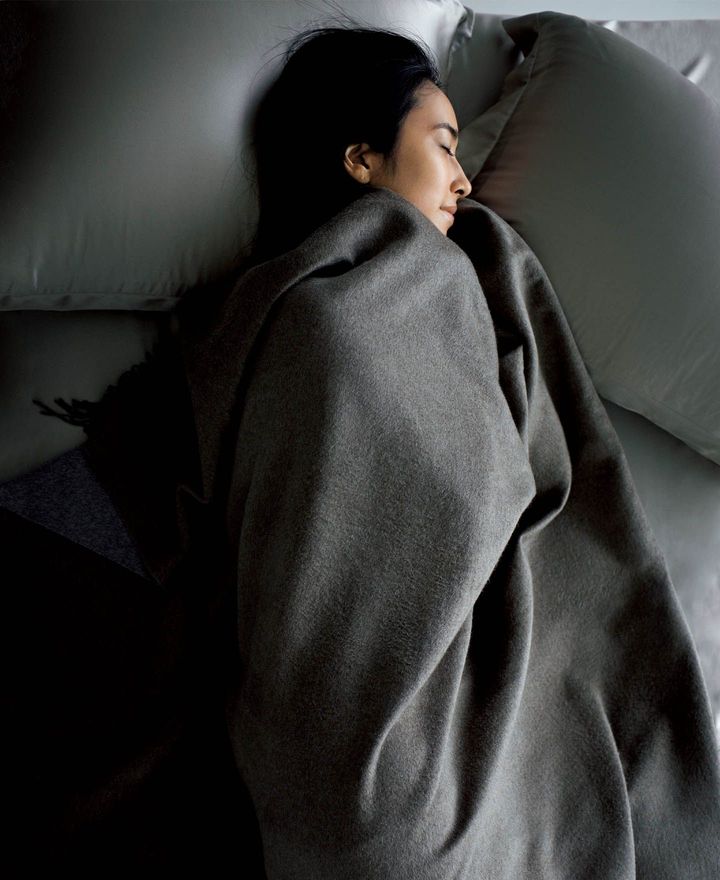 モカブラウンとグレー、シックな配色が穏やかなリラックス感を誘うダブルフェイスのシルクブランケットは、フリンジがチャームポイント。コクのある艶とリッチな風合い、じんわり肌に伝わる温もりが上質さを物語る。肌や髪との摩擦が気になる枕カバーやシーツはなめらかなシルクサテン素材。タッチで使い分けるのが賢い大人の選択。ブランケット［約150×180㎝※編集部計測］￥162,800（ブルネロ クチネリ ジャパン）