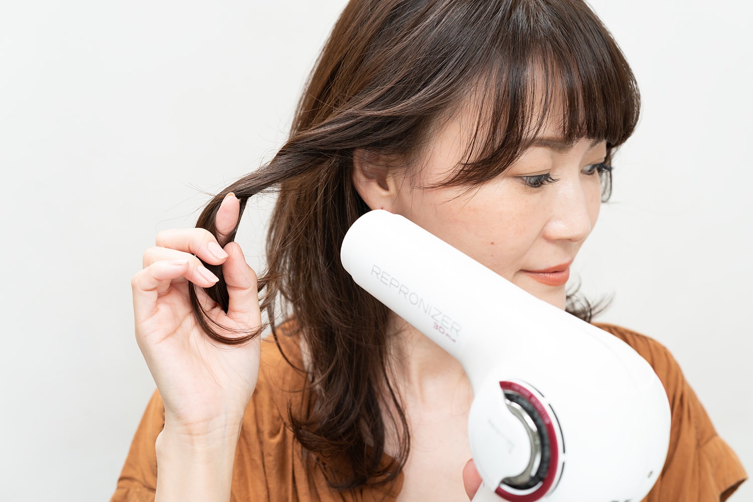 顔周りの髪を指に巻きつけてドライヤーの熱を当てる。耳の後ろに向けて熱を当てると、肌の露出が増えて抜け感ができる。