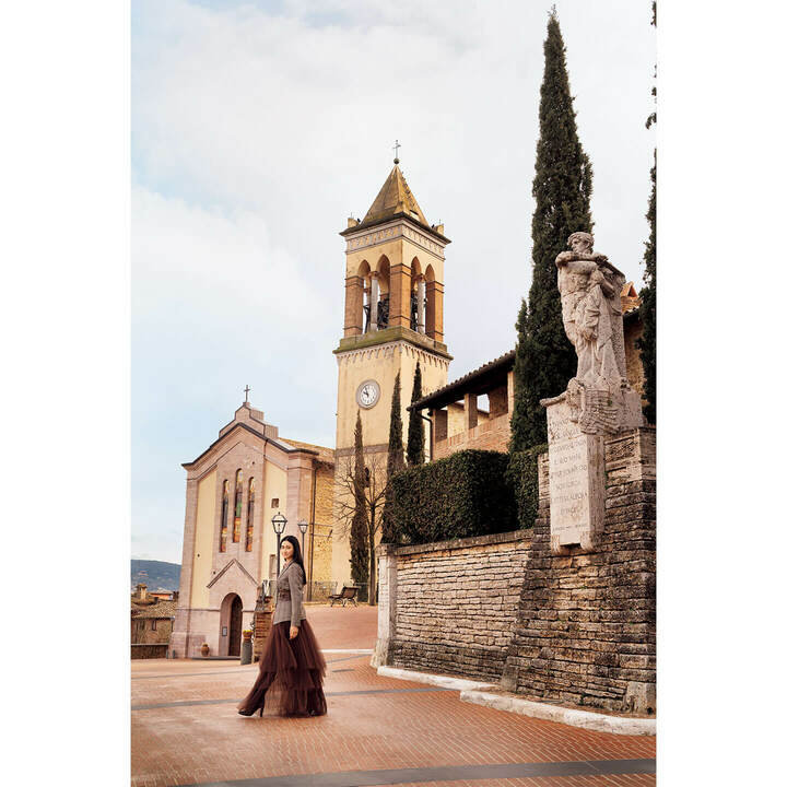 小高い丘にある教会前の広場にて。古い石やレンガ造りの街並みがボルドーのスカートに溶け合い、美しく共鳴しています。ジャケット￥490,000・シャツ［参考商品］・シフォンスカート￥253,000・ベルト￥156,000・靴［参考商品］（ブルネロ クチネリ ジャパン）