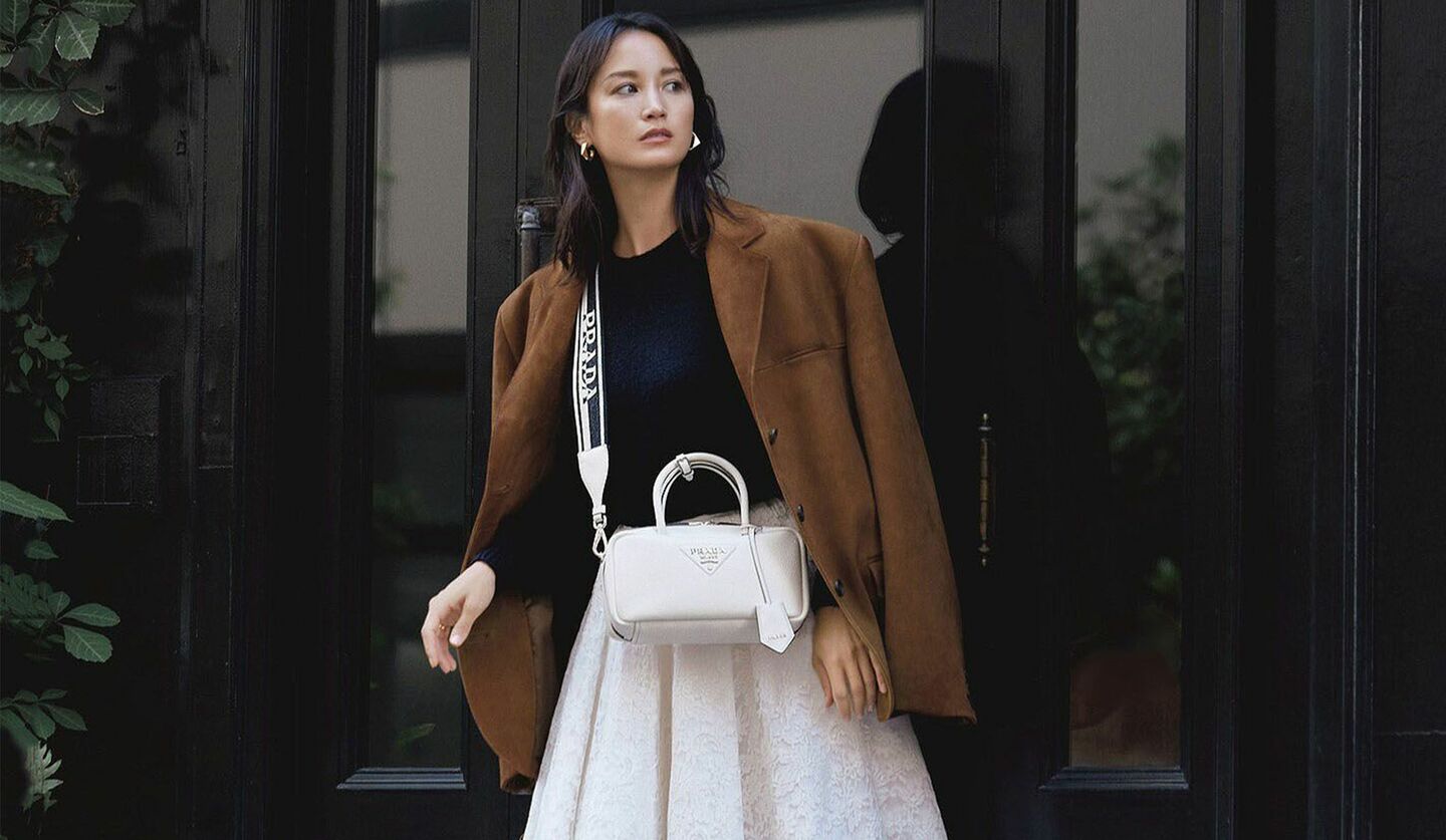 ブラウンジャケットに白のスカート、プラダの横長ホワイトのバッグのコーデを着るモデルの黒田エイミさんの写真