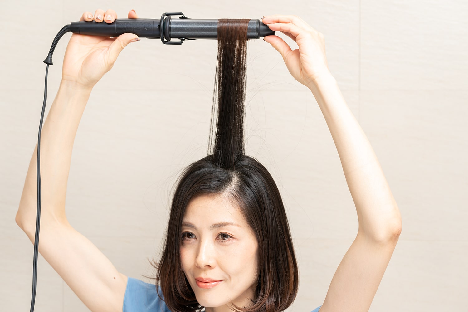 頭頂部の毛束をざっくりと取って中間に巻きつけたら、毛先に向かってコテを滑らせるように通す。上に向けてコテを抜くようなイメージで。
