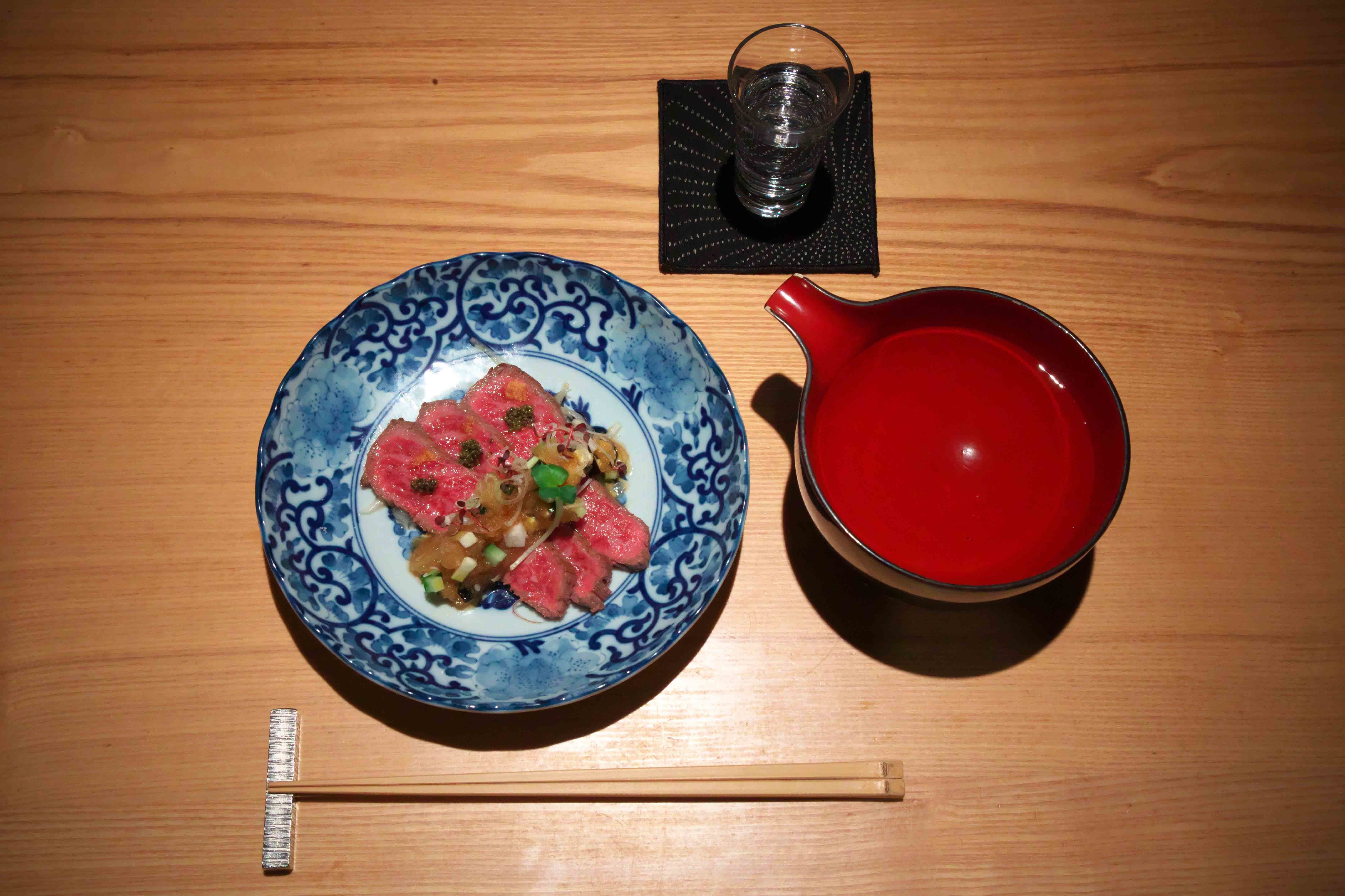 柔らかい赤身のイチボで、刻んだキュウリやなすの食感もいいおろしのタレをくるりと巻いて頬張る。これが旨い!「和牛A5イチボ叩き」通常価格¥2,200。写真は深夜のひとり飯にちょうどいいハーフサイズ。漆塗りの片口は、下北沢の創業時代から使っているもの。懐かしく感じる長年の常連客も多いという。