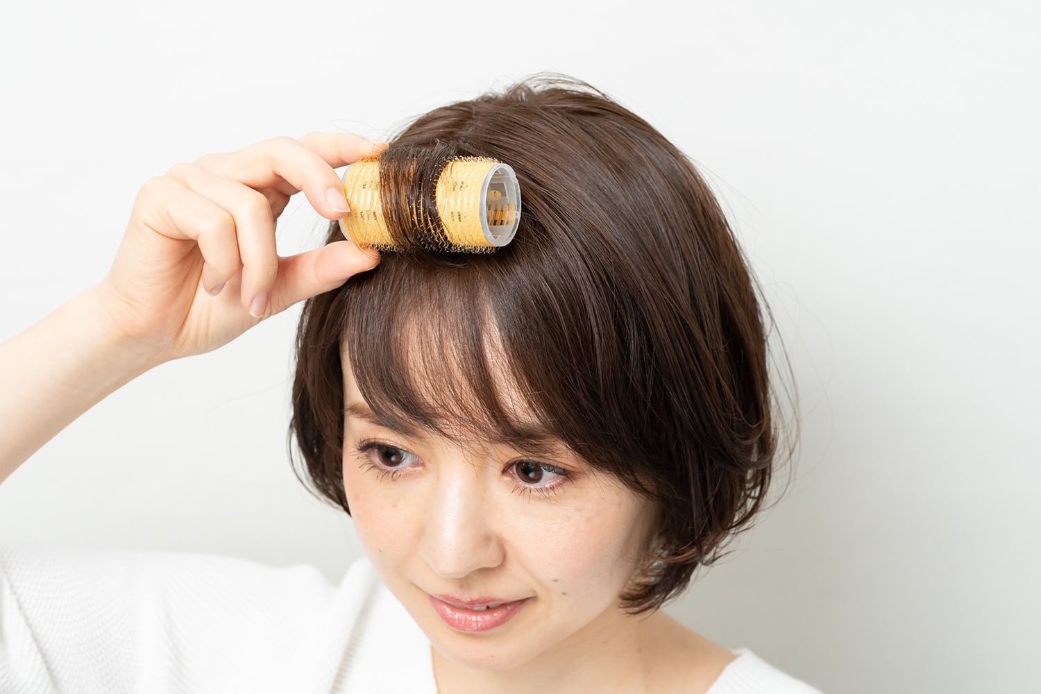 分け目をまたぐように毛束をとり、カーラーで巻く。