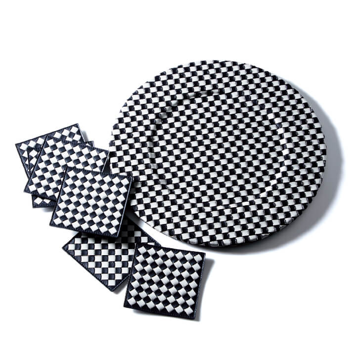 2018年4月のミラノ・サローネ国際家具見本市で注目を集めた、モノトーンのチェッカー柄仕上げの「イントレチャート」。テーブルアイテムは、合わせるグラスや食器、花などでアレンジを楽しめるのが魅力。チャージャープレート（ディナープレートの下に敷く化粧皿）［直径30cm］￥67,000・コースター［6枚セット］￥39,000（ボッテガ・ヴェネタ ジャパン）　[Precious2019年1月号220ページ] 