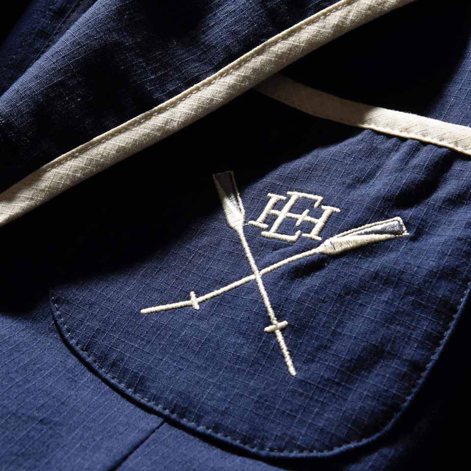 胸ポケットには、ブランドの文字を型どったロゴとオールの刺繍があしらわれている。