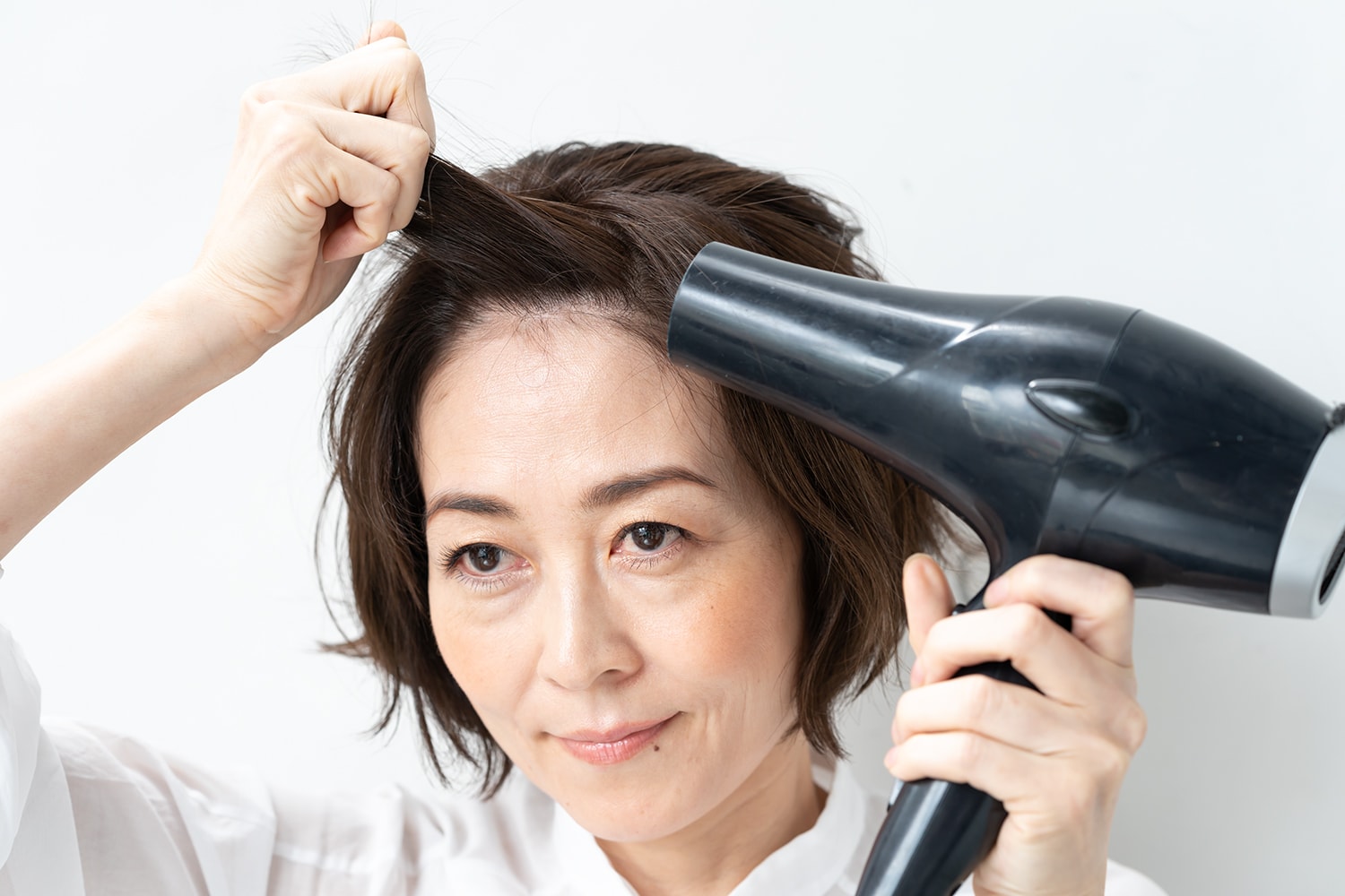 前髪を持って、両サイドからドライヤーを当てる。いつもの分け目と逆に髪を降ることで前髪の割れを防ぐことができます。