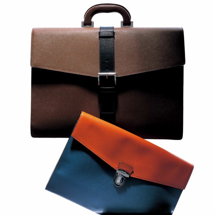 同社の伝統的な素材、「サフィアーノ」レザー（カーフの型押し）が採用されたブリーフケース。クラシックなスタイルでありながら、センターにベルトを配する事で、新鮮かつモードなビジネスバッグが誕生した。クラッチバッグは、定番で展開するモデルの新色。上［縦31×横43×マチ12㎝］￥280,000・下［縦26×横36㎝］￥147,000／ともに予定価格（プラダ ジャパンカスタマーリレーションズ）