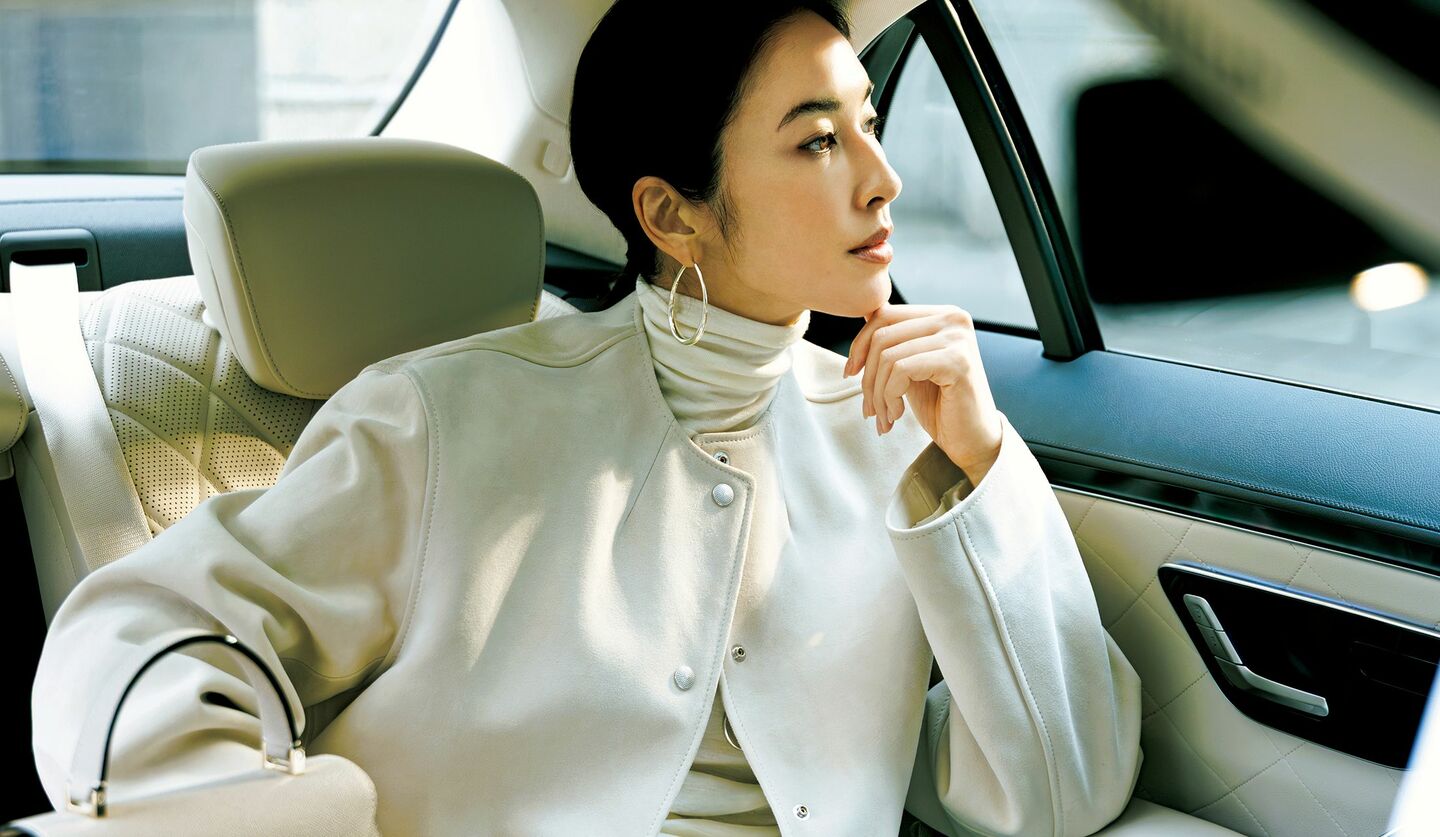 自動車内に座る、ホワイトのジャケットとニット、パンツを着用したモデル