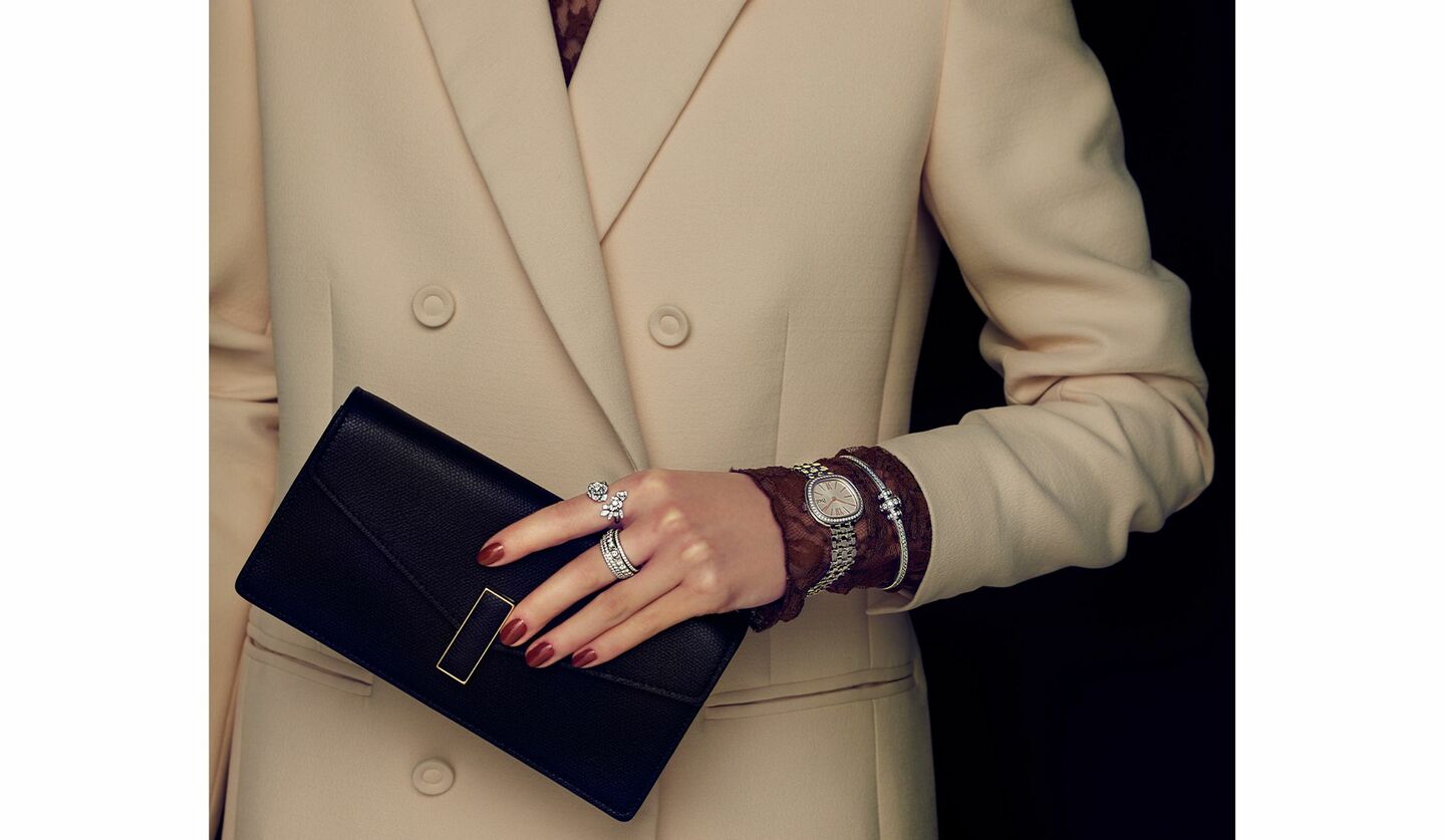 「ヴァレクストラ」のクラッチバッグと「ピアジェ」のジュエリーを纏った女性の手元