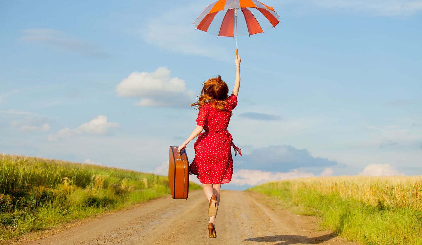 旅行カバンと傘を持つ赤い服を着た女性