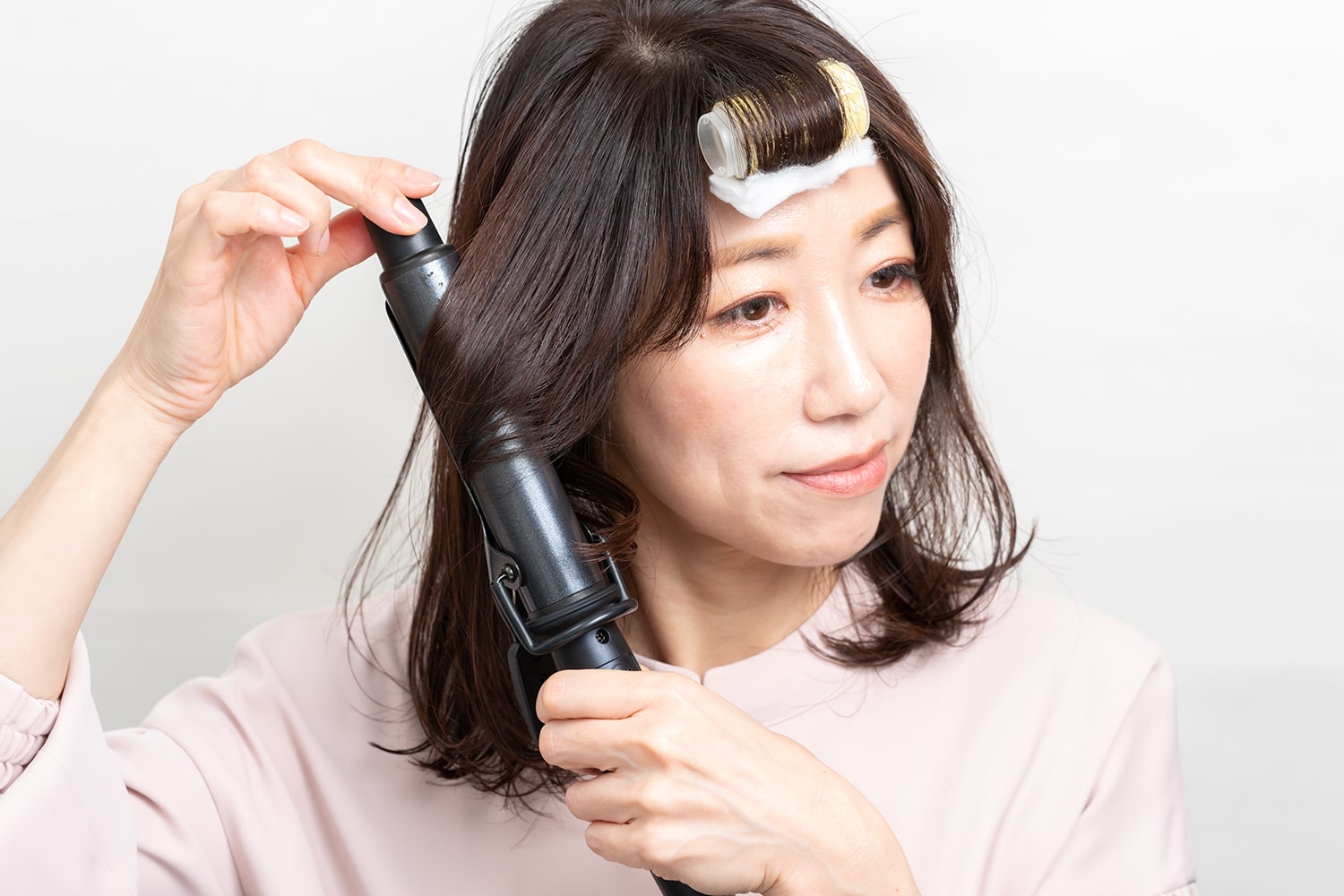 顔まわりの毛束をざっくり取ってリバース巻きに。毛束の中間を巻くイメージで。