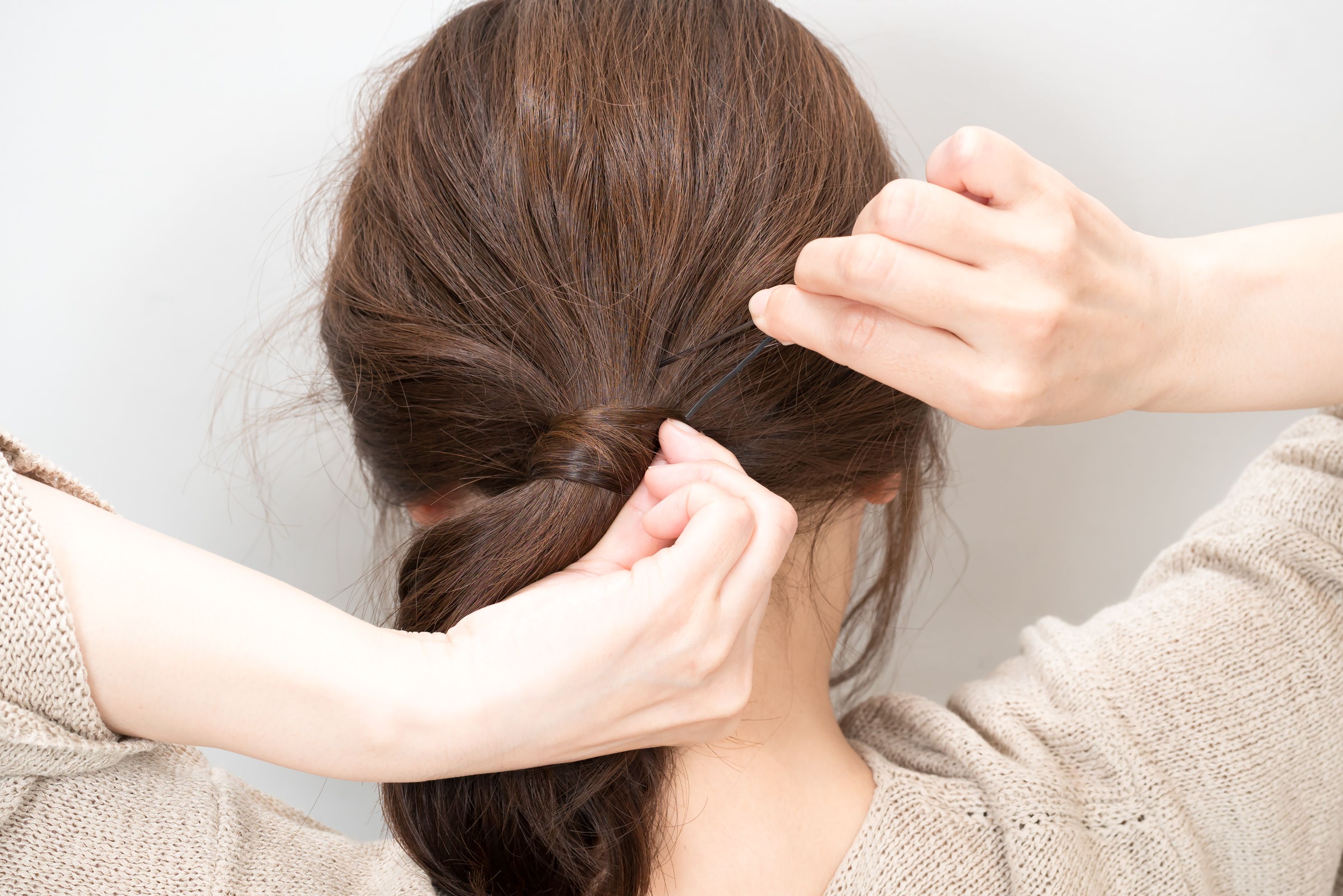 巻きつけた髪の毛先を崩れないようにピンで止める。ポニーテールの下に止めると、ピンがきれいに隠れる。