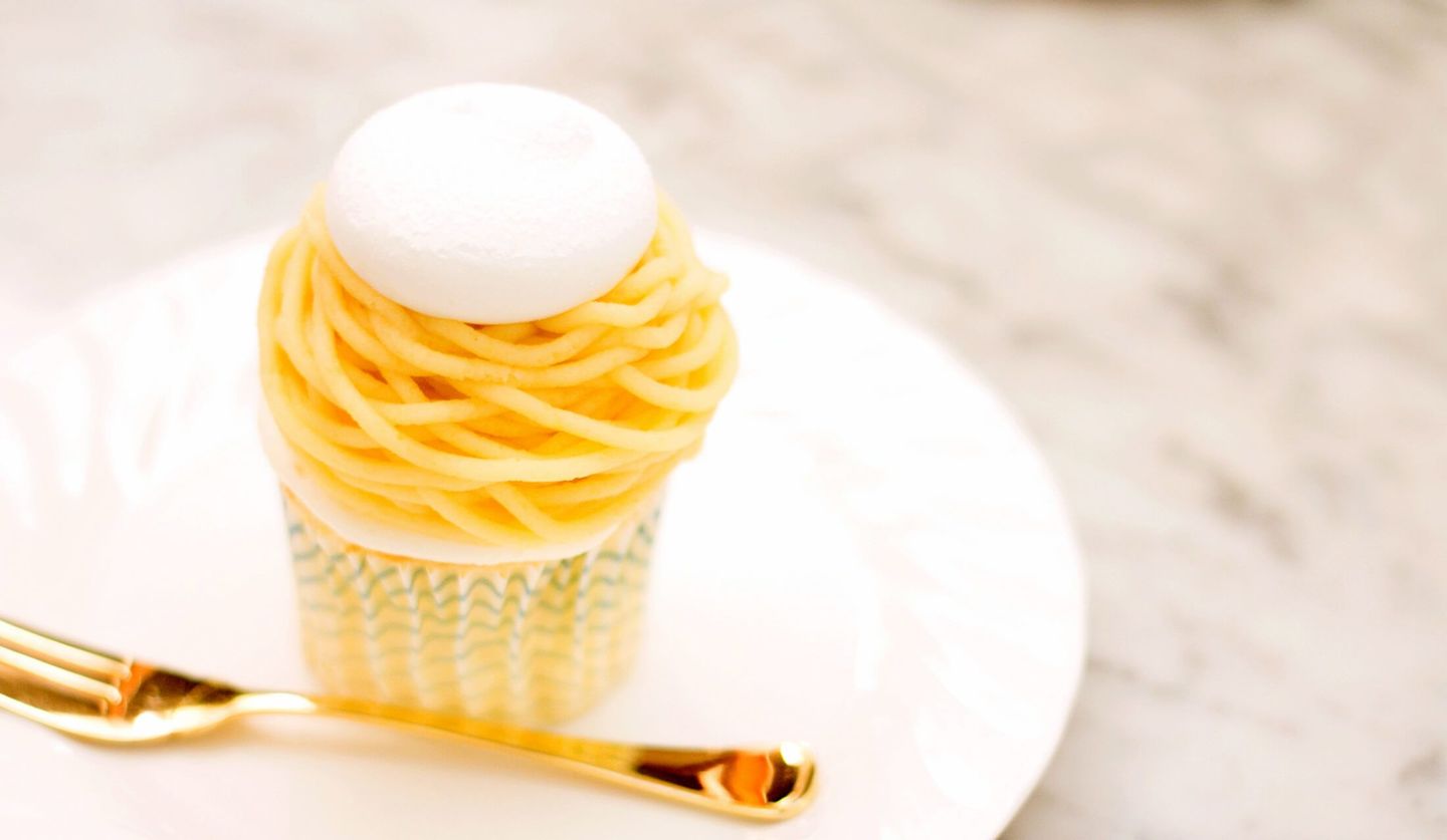 黄色のマロンクリームに白いメレンゲが乗ったモンブランが白いお皿に置いてあり、金色のフォークが添えてある