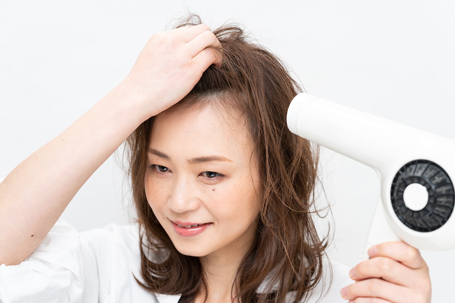 分け目をまたぐように、頭頂部の髪を真上につまみ上げ、ドライヤーを根元にあてる。