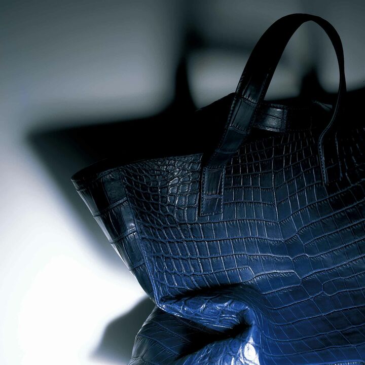 エキゾチックレザーのなめし、染色、製鞄までの工程をすべて自社生産するスペシャリストがつくるトートは、芯地に一般的には使用されない床とこ革がわ（銀面がつかない下層部分の革）を採用。見た目には決してわからないが、使い込むほど本体の革となじみ、持ったときの安定感も別格。しかもこのクオリティと手仕事でこの価格は、感動的！［縦29×横38×マチ10㎝］￥360,000（山本製鞄）