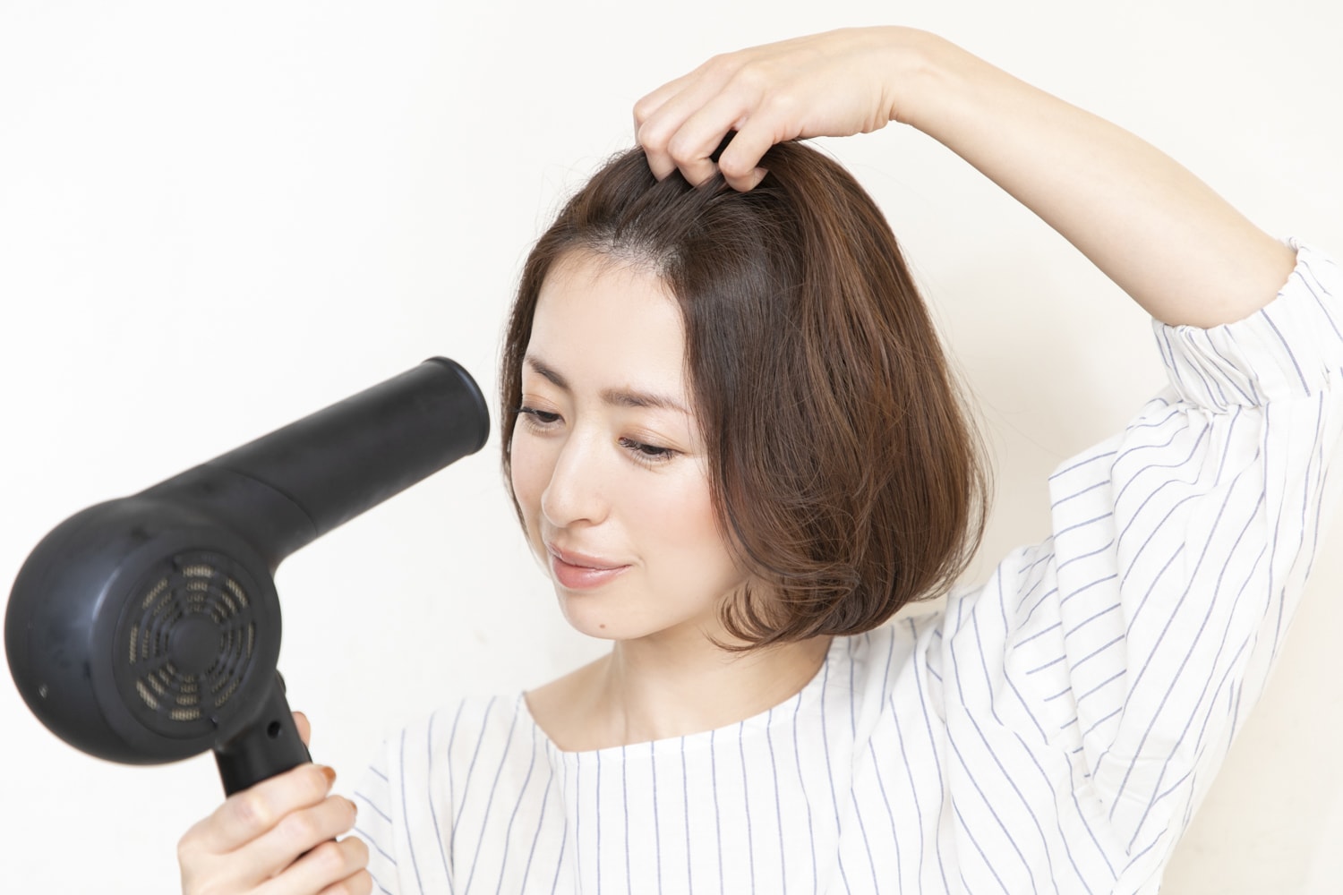 前髪を持ち上げ、根本にドライヤーで温風を当てる。