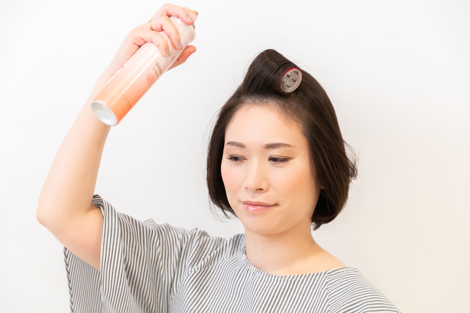 トップの前髪を、マジックカーラーで後ろ向きに根元まで巻き、ライトタイプのキープスプレーを吹きかける。