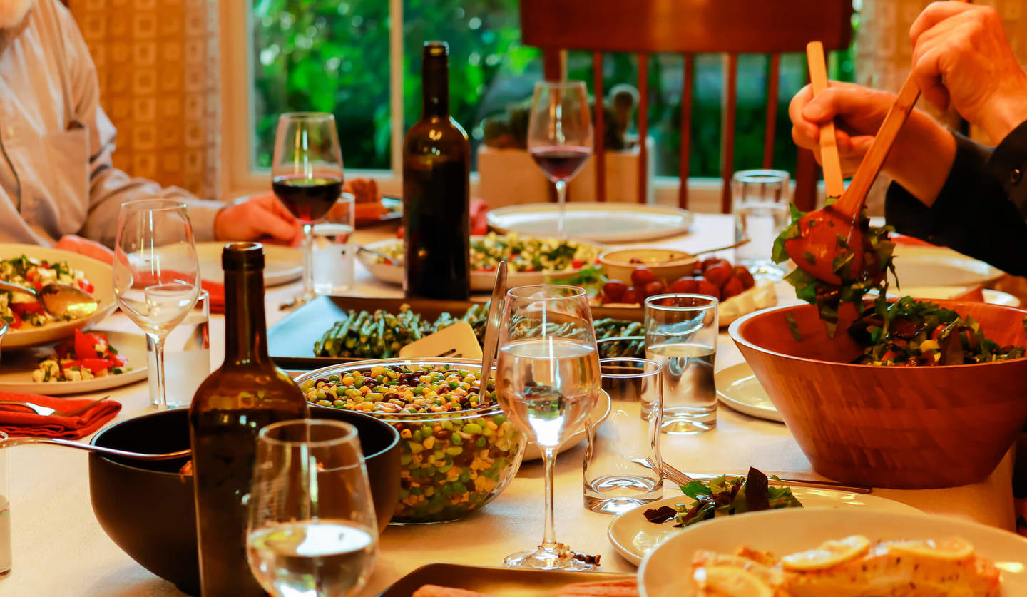 赤ワインやサラダなどがテーブルに上に乗せられ、1名がサラダをお皿へ盛り分けている様子