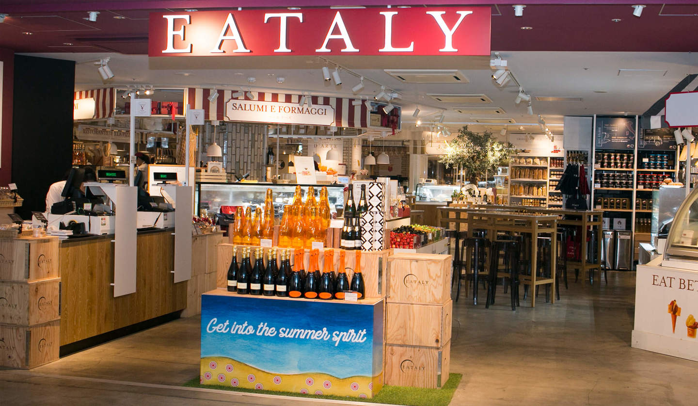 イータリー グランスタ丸の内店店舗正面。臙脂の天井、木箱の上にワインが並ぶ。中央上に「EATALY」の文字