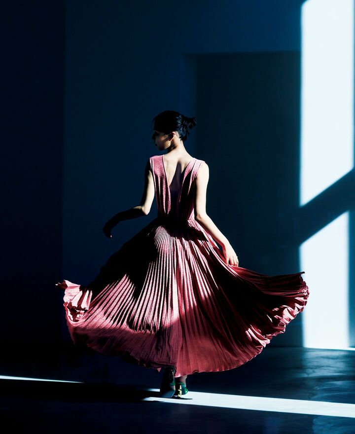 シェイプされたウエストからプリーツが華やかに広がるフィット＆フレアのエレガントなシルエットを、適度なウェイトとハリのあるジャージー素材で仕立てたドレスは着心地抜群。甘やかなローズピンクをベースにしながらも、気品溢れるシルバーラメがダイヤモンドダストのように眩く煌めく。品よくコンフォタブルにドレスアップが叶う一着。ドレス￥407,000／予価・ピアス［YG×タンザナイト×ペリドット］￥462,000・靴￥170,500／予価（ドルチェ&ガッバーナ ジャパン）