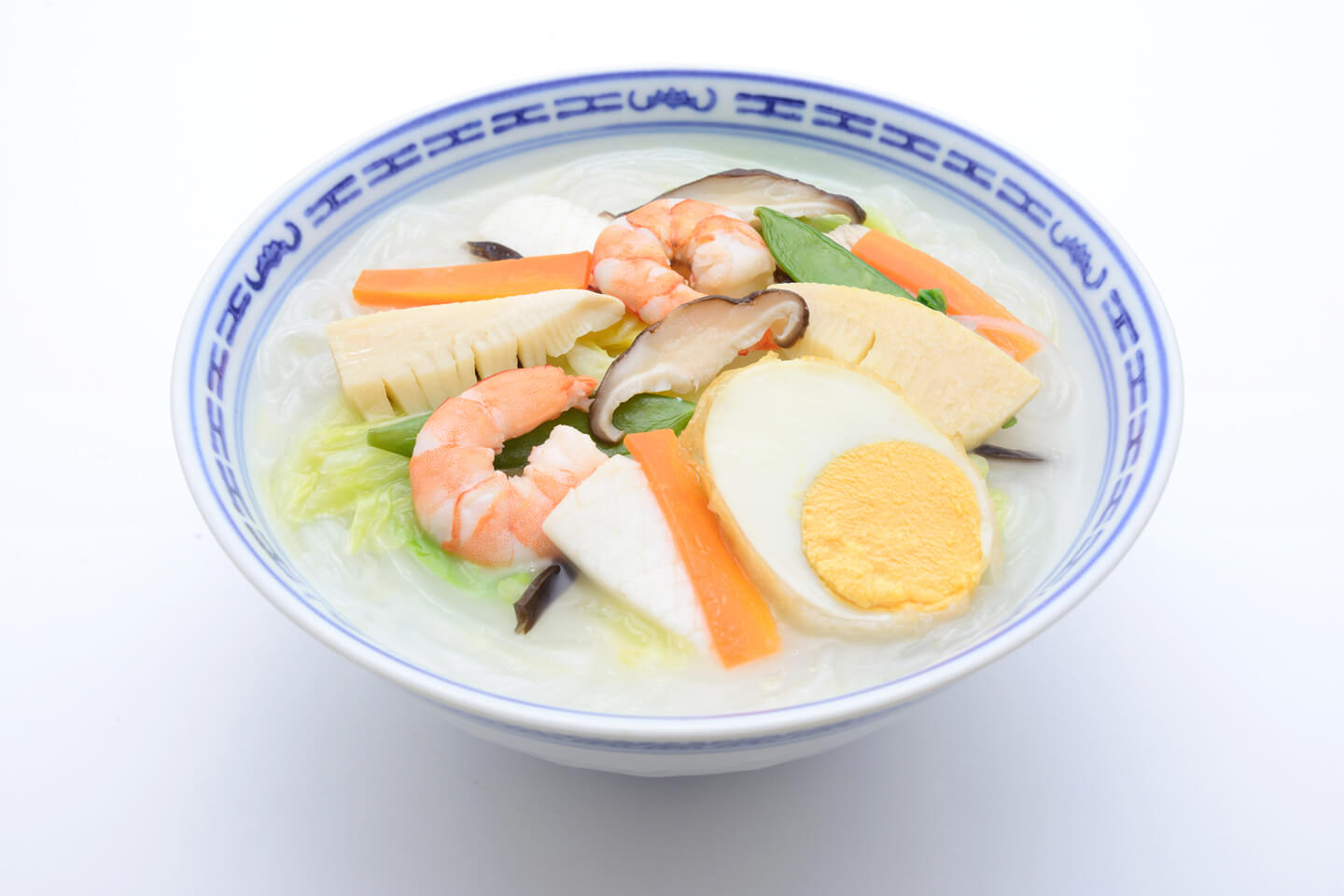 透明な麺と白濁色のスープの上にキャベツや筍、エビやイカ、半分に切られた揚げ卵が盛られている