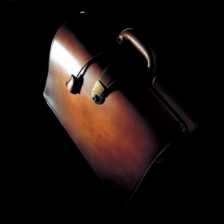 イタリアンショルダー（成牛の肩の部分）を採用したダレスバッグは、側面と底面にプレートを入れ強度を持たせた独自の構造。モノの出し入れを容易にする大きく開いた開口部は、流れるような曲線が実にエレガント。一点一点手染めし、総手縫いでつくられるため、オーダーから４～５か月を要する。美意識の高い技術を持った職人による磨き直しサービス（有料）も実施。［縦30×横44×マチ14㎝］¥420,000（ユハク）