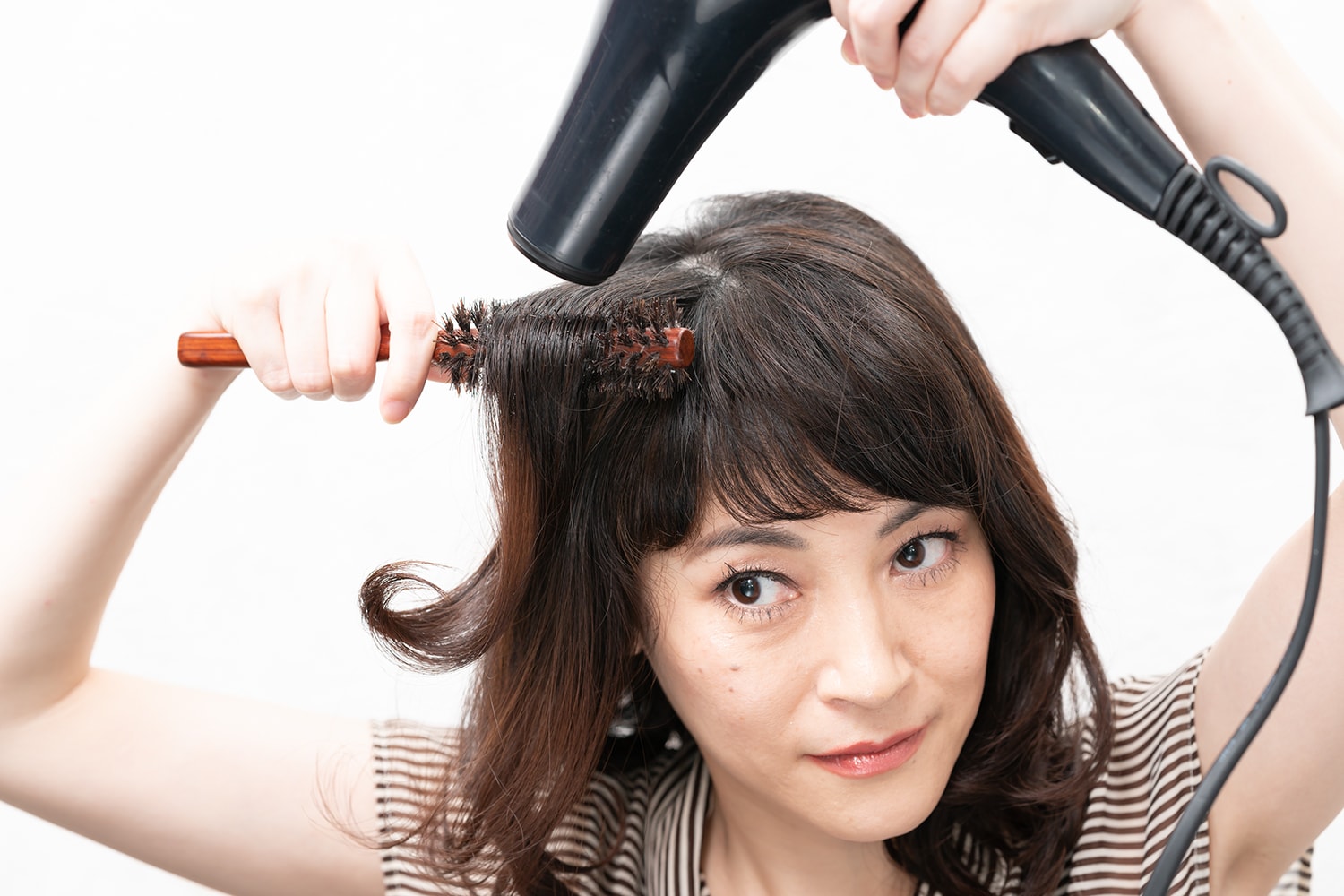 耳前の毛束(前髪以外)をブラシでブローしながらドライヤーの熱を当てる。逆サイドも同様に。毛束の根元から中間にドライヤーを当てるのがポイント。