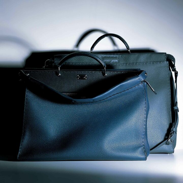 ハンドルは、ドクターズバッグから着想した堅牢なつくり。開口部の片側は、ファスナー開き仕様で、ビジネスシーンにもふさわしいシンプルなデザイン。カジュアルにも持てるショルダーストラップ付き。手前（ネイビー×ブラック）は、定番よりひとまわり小ぶりサイズ［縦31.5×横41×マチ16.5㎝］¥613,000・奥（グレー×ネイビー）［縦35.5×横43×マチ20.5㎝］¥646,000（フェンディ ジャパン）　※写真右は、『ピーカブー』を始めとする同社の革小物に共通して使用できる、専用のケアクリーム¥8,000（フェンディジャパン）