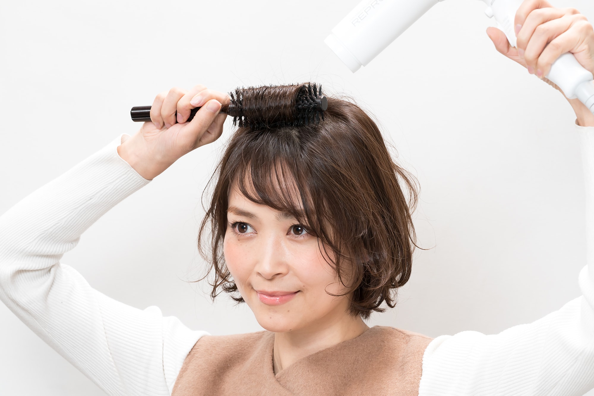 頭頂部の髪を根元からロールブラシで内巻きにし、ドライヤーを3秒ほどあてる。ドライヤーの熱が冷めるまで、5~10秒ほど巻いたままキープ