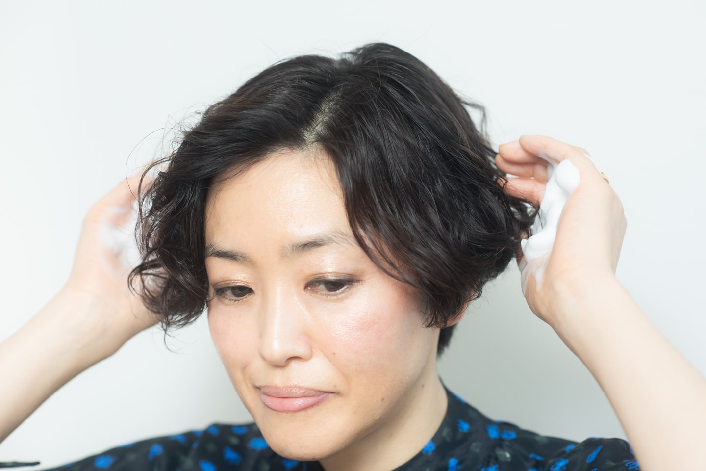 髪が濡れた状態でスタート。保湿力のあるトリートメントムースを手のひらに取り、髪全体にもみこんでパーマを出す。