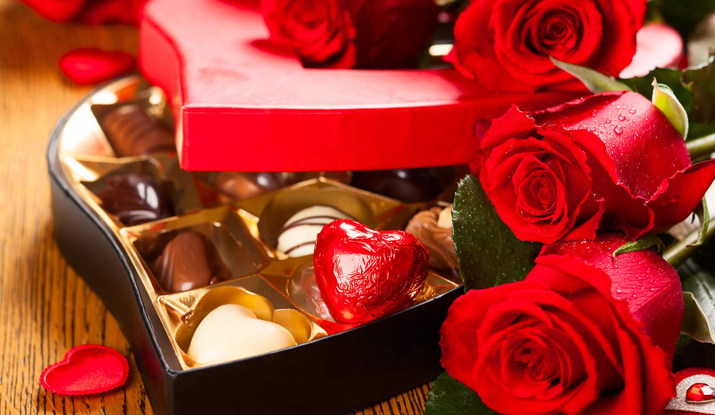 ひと口サイズのチョコレートが複数入っているハート形の箱の周りに、赤いバラが添えてある